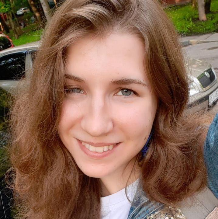 Alexandra has auburn hair in this image, blue eyes and she smiles into the camera.